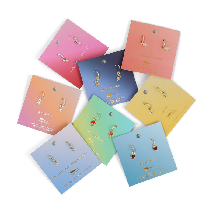 Several pairs of gold hoop earrings with different charm designs are displayed on colorful cards.