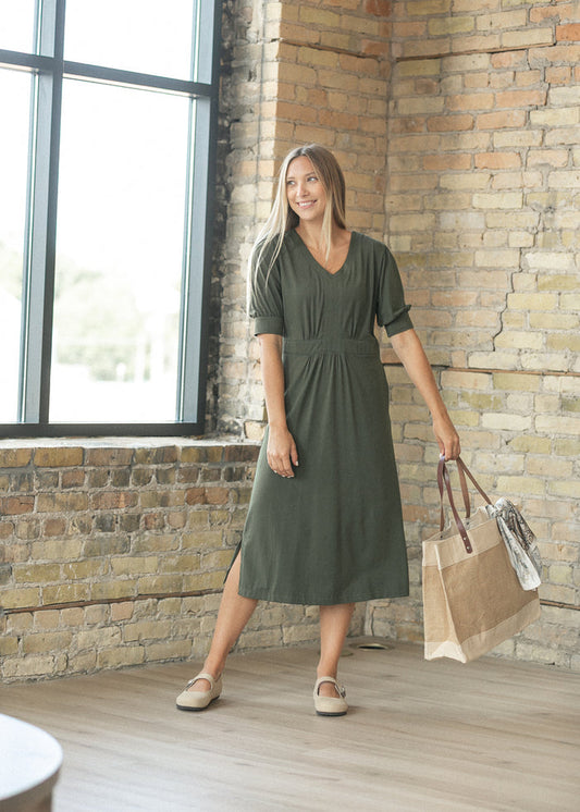 Deep olive green puff sleeve midi dress with a side slit, carried with a woven jute tote.