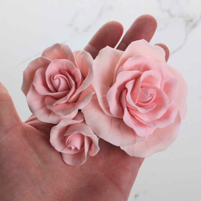 Hand holding three handcrafted pink sugar garden roses showing assorted size comparison and petal details by Caljava