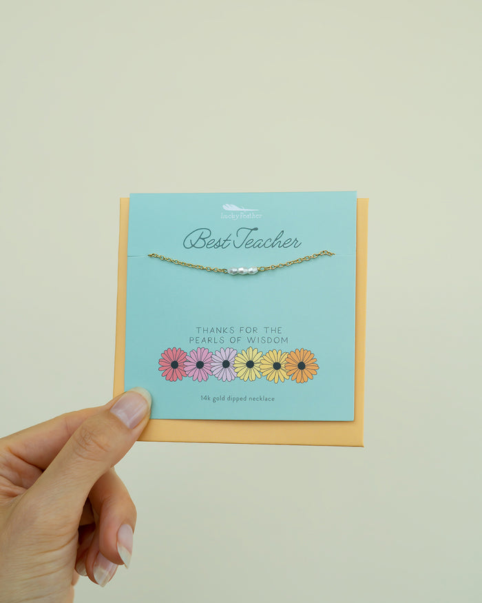 A hand holds a card that displays a gold necklace with pearls, a 'Best Teacher' message, and flower illustrations.