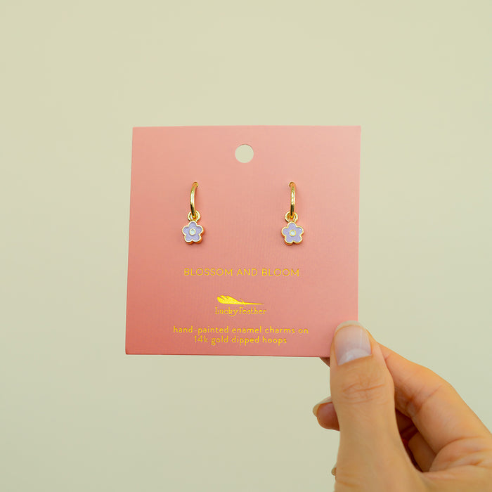 A hand holds earrings displayed on a pink card.