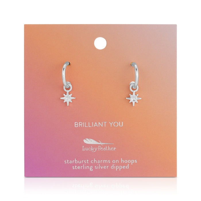 A pair of sterling silver dipped hoop earrings with starburst charms on a 'Brilliant You' Lucky Feather display card.
