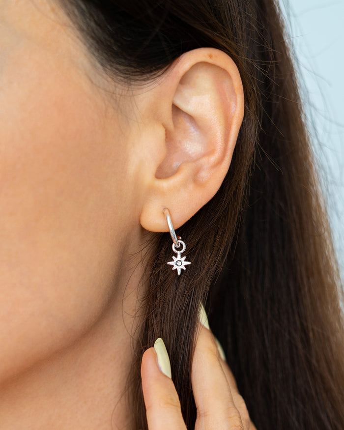 A silver hoop earring with a starburst charm hangs from a woman's ear.