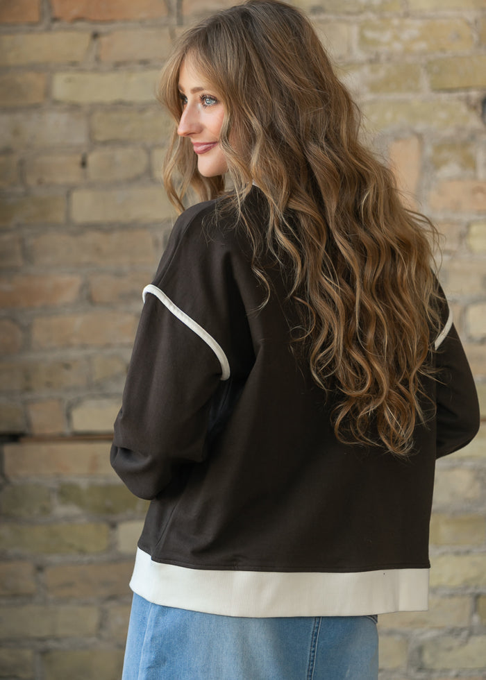 Back of espresso crewneck sweater showing drop shoulders and cream contrast hem and sleeve trim.