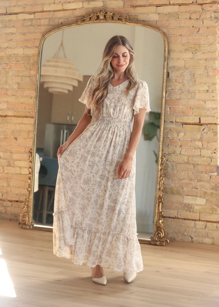 Cream floral maxi dress with a modest V-neck, flutter sleeves, and smocked waist detail.