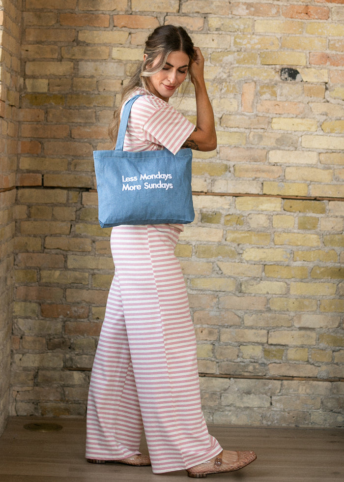 Denim tote bag with white embroidered lettering, styled over the shoulder with a pink striped set.