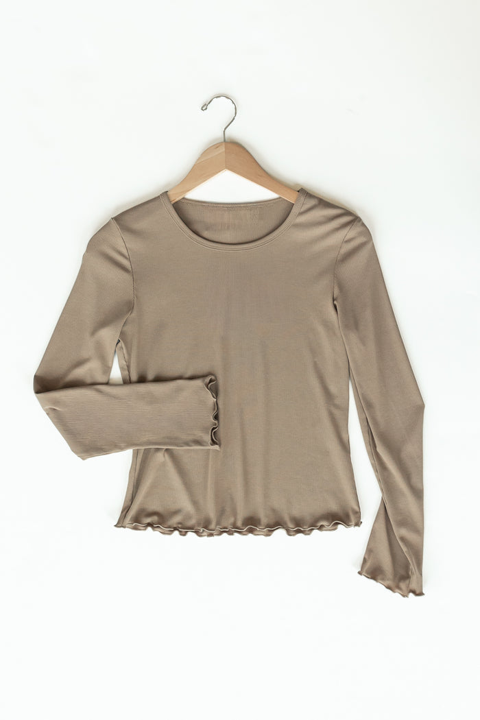 A taupe long-sleeve top with a ruffled hem and buttoned cuffs, hanging on a wooden hanger against a white background.