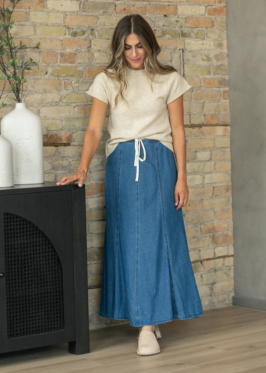 Blue denim maxi skirt with drawstring waistband, paneled construction, and full flowing hem.