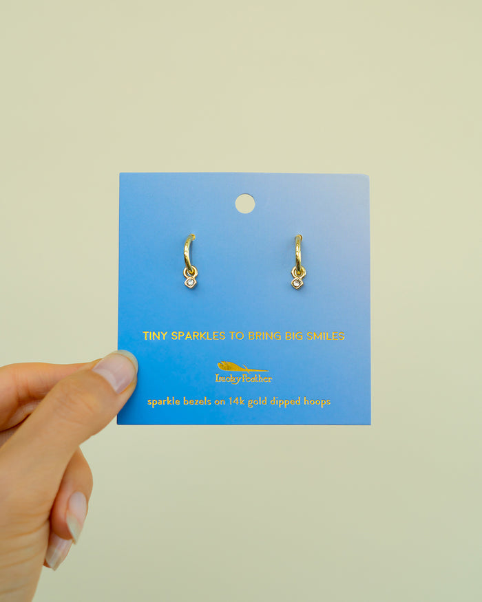 A hand holds a blue display card with gold hoop earrings attached.